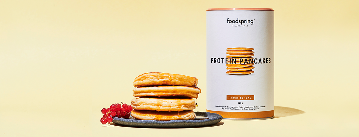 A canister of Protein Pancakes sits next to a stack of fluffy pancakes
